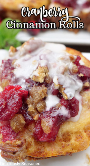 A close up of a cinnamon roll with cranberries and a brown sugar pecan crust with icing over it.