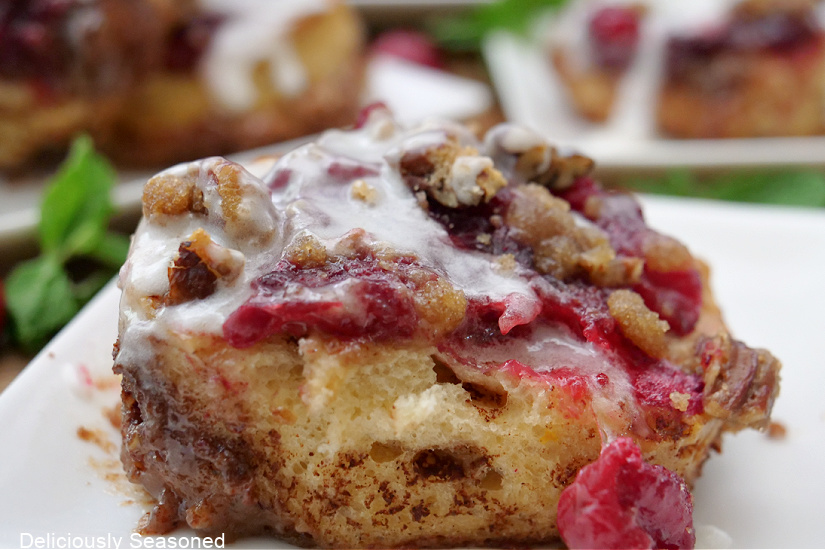A close up of a cinnamon roll topped with a cranberry orange topping and a brown sugar pecan crust.
