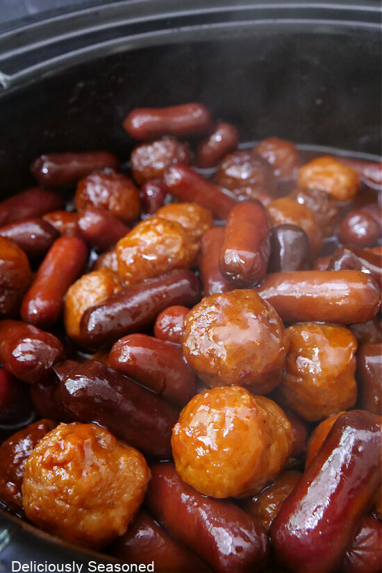 A close up photo of a crockpot filled with meatballs and little smokies.