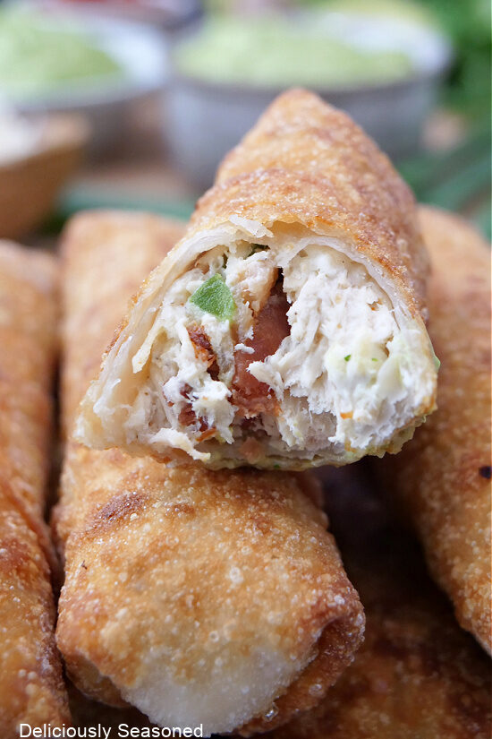 A small stack of egg rolls with one that has a bite taken out of it.
