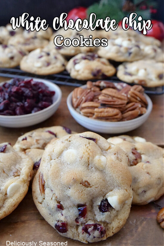 A few white chocolate chip cookies with cranberries and pecans on a wood surface with more cookies in the background.