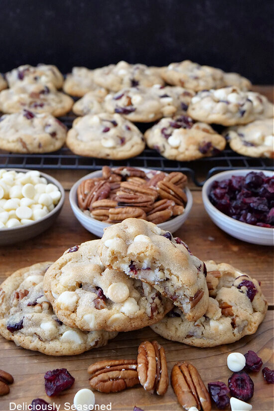 A wood surface with cookies, pecans, white chocolate chips, dried cranberries on it.
