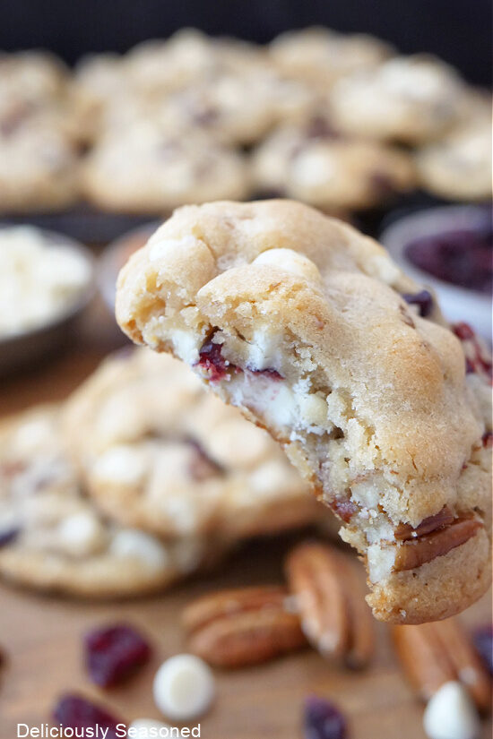 A close up of a white chocolate chip cookie with cranberries and pecans that has a bite taken out of it.