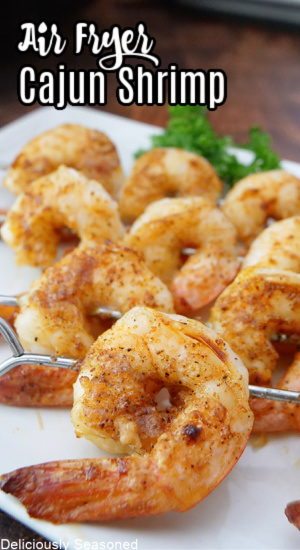 A white plate with shrimp on metal skewers placed on it.