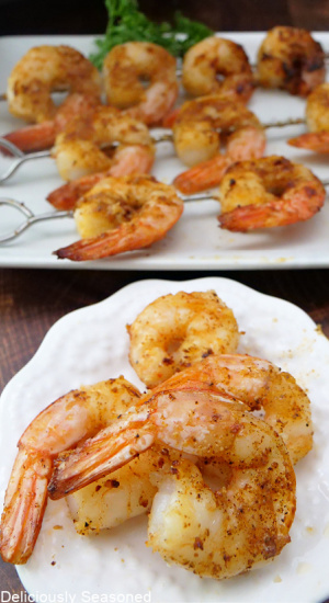 A round white plate with 4 shrimp on it and another plate in the background with shrimp of skewers.