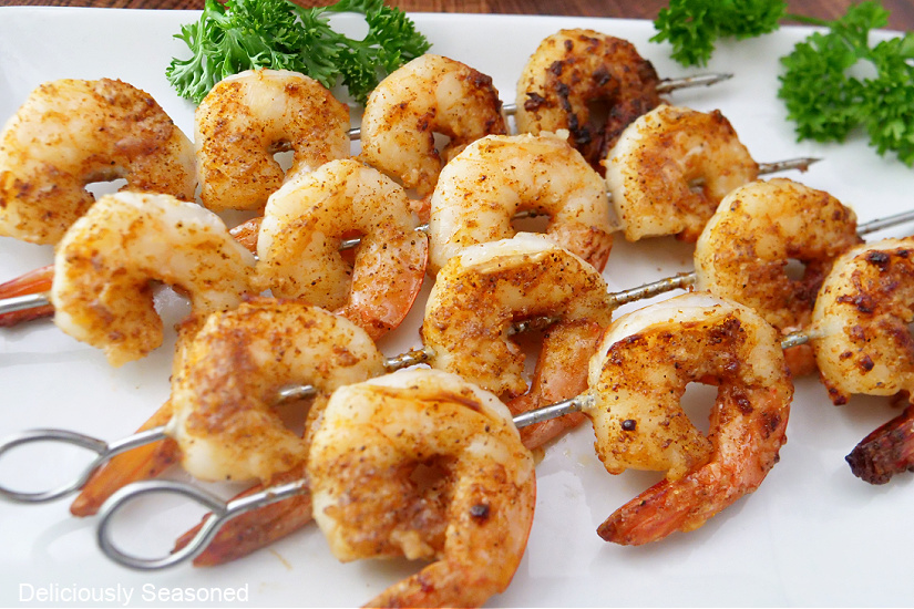 Four metal skewers on a white plate with Cajun shrimp on them.