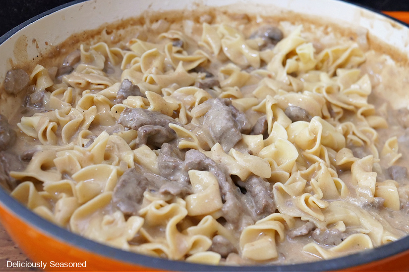 An orange cast iron pan with beef stroganoff in it.