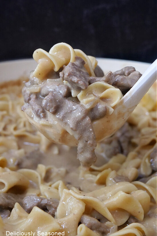 A ladle full of beef stroganoff being scooped out of the pan.