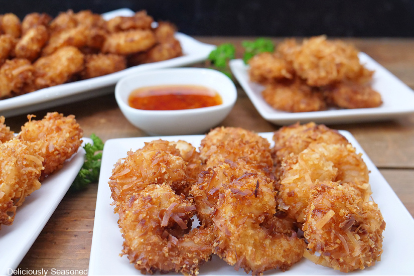A horizontal photo of four white plates with coconut shrimp on them.