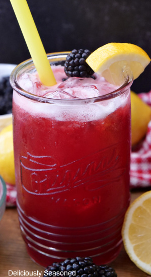 A close up picture of blackberry lemonade in a glass cup with a yellow straw.