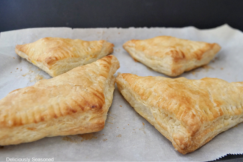 Four breakfast turnovers on a piece of parchment paper. 