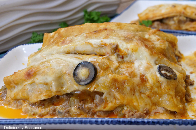 A horizontal photo of a beef enchiladas on a white plate with blue trim.