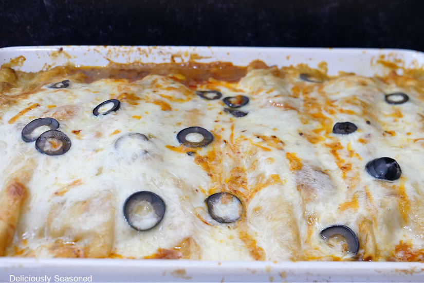 A horizontal photo of a white casserole dish filled with cheesy beef enchiladas.
