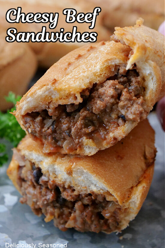 French roll stuffed with ground beef, cheese, onions and more that is cut in half on a sliver tray.