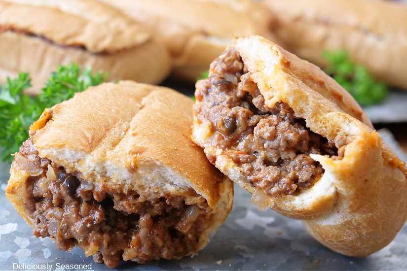 A horizontal photo of a French roll filled with seasoned ground beef, cheese and more cut in half and one half leaning of the other.