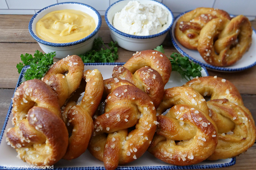 A long white plate lined with soft pretzels and a small bowl os cheese dip and another of cream cheese in the background.