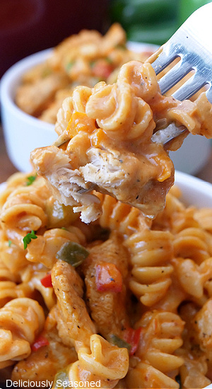 A bite of one pot creamy chicken pasta on a fork held above a bowl of pasta.