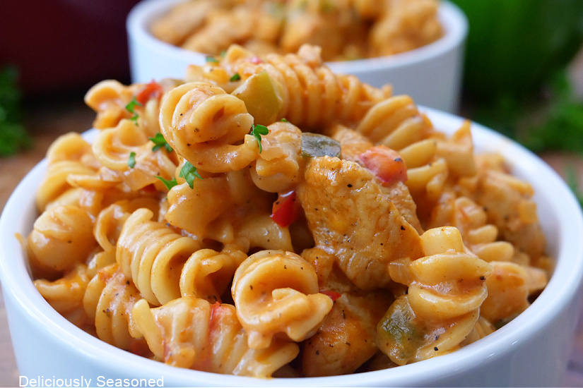 A close-up horizontal photo of chicken and pasta in a white bowl with another filled bowl in the background.