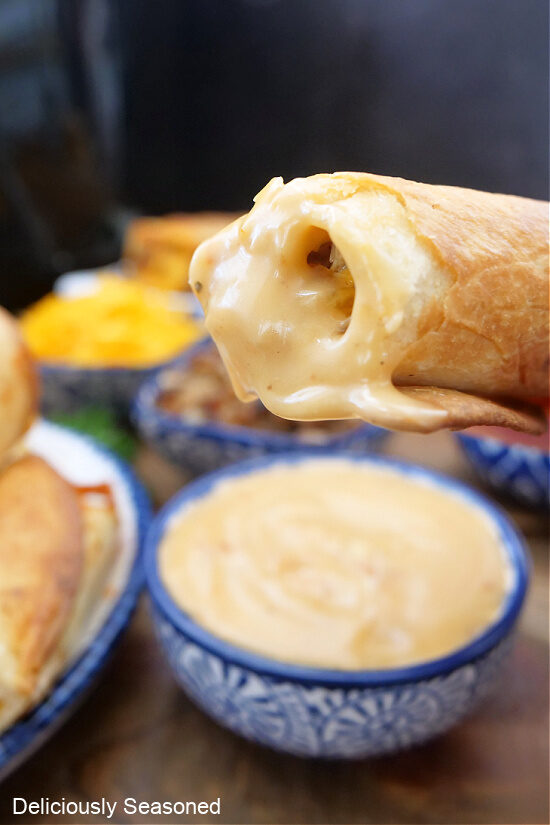 A chicken flautas that has been dipped in cheese sauce.