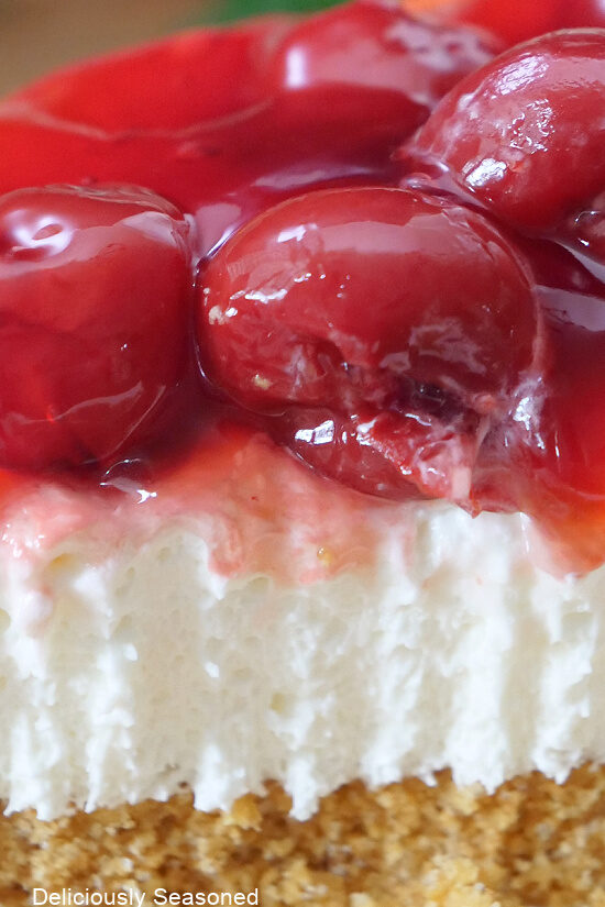 A close up photo of cherry dessert showing the graham cracker crust, a layer of cream cheese, and cherry pie filling on top.