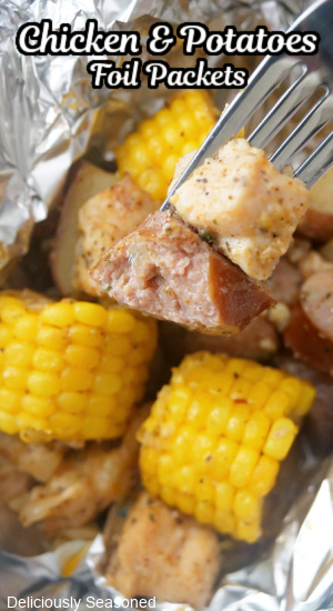 A fork with a piece of sausage and chicken on it with corn and potatoes in the photo.
