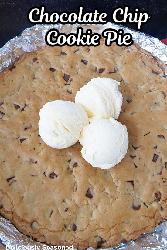 A giant chocolate chip cookie pie in a cast iron skillet lined with foil with three scoops of vanilla ice cream on the cookie.