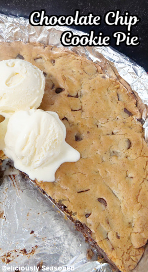 A photo of a skillet cookie pie with a few scoops of vanilla ice cream with a slice taken out of it.