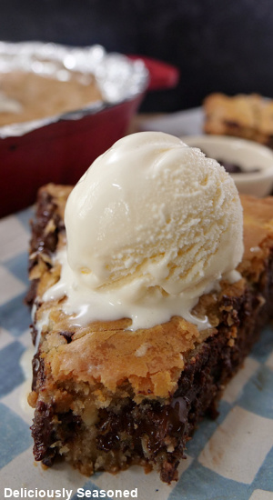 A slice of cookie pi on a white and blue checkered plate with a scoop of vanilla ice cream.