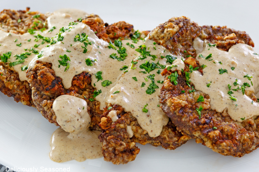 A horizontal photo of fried cube steak with gravy on a white plate.
