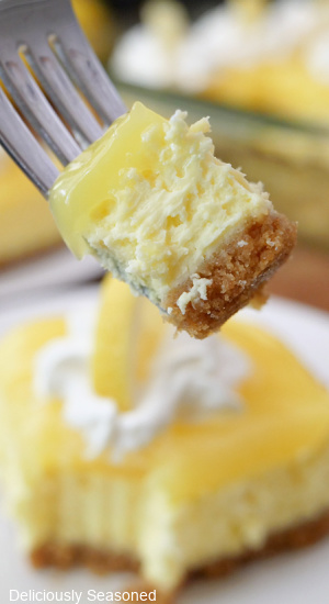 A close up of a fork with a bite of lemon cheesecake on it.
