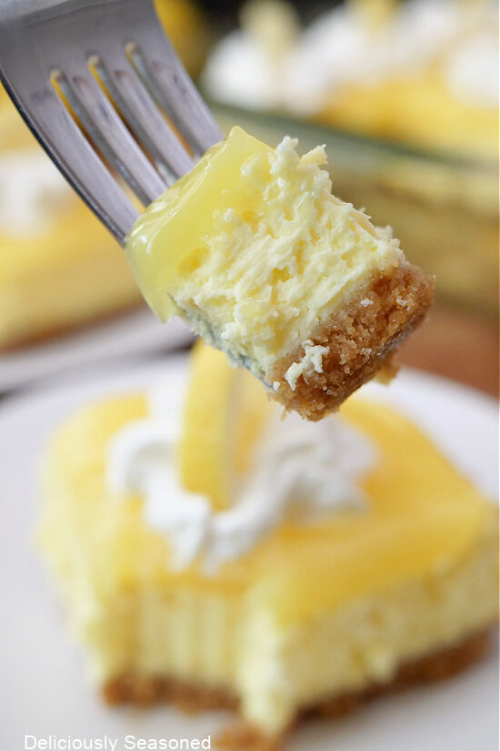 A close up of a bite of lemon cheesecake bar on a fork being held close to the camera lens.