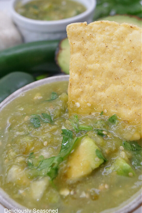 A close up of a tortilla chip being dipped into the salsa verde.