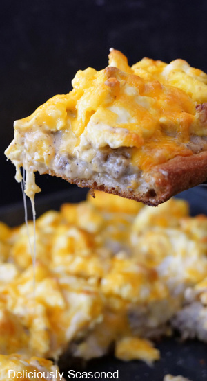 A slice of breakfast pizza held up close to the camera lens.