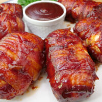 A close up of a few bacon wrapped chicken bombs on a white plate.