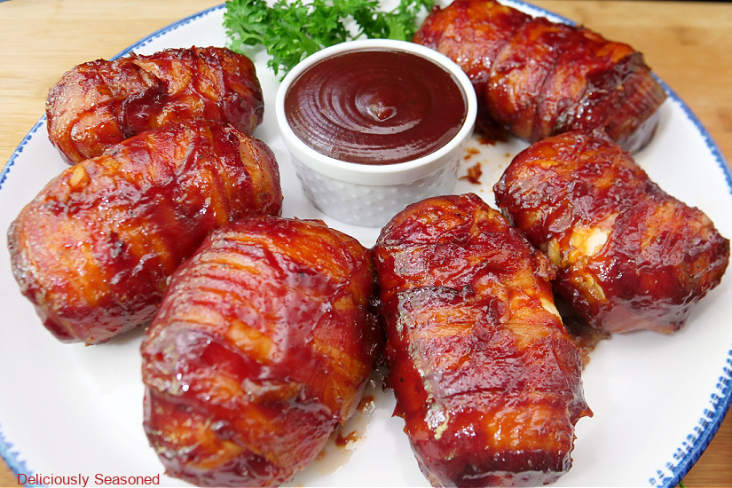 A horizontal photo of a white plate with blue trim with six chicken bombs on it with a small white bowl filled with BBQ sauce.