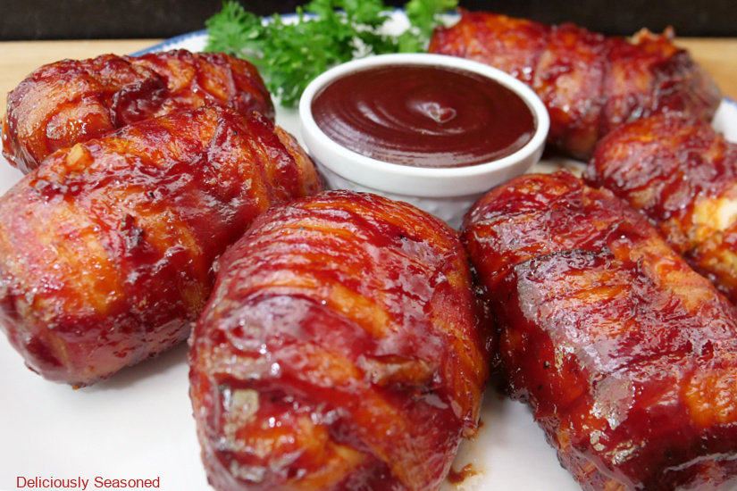 A horizontal photo of six chicken bombs on a large white plate with a small bowl of barbecue sauce in the center of the plate.