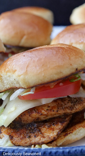 A close up of a toasted slider bun with two pieces of grilled chicken, cheese, tomato and lettuce on it.