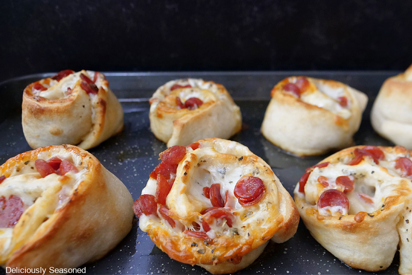 A baking sheet with pepperoni pizza pinwheels on it right after being removed from the oven.