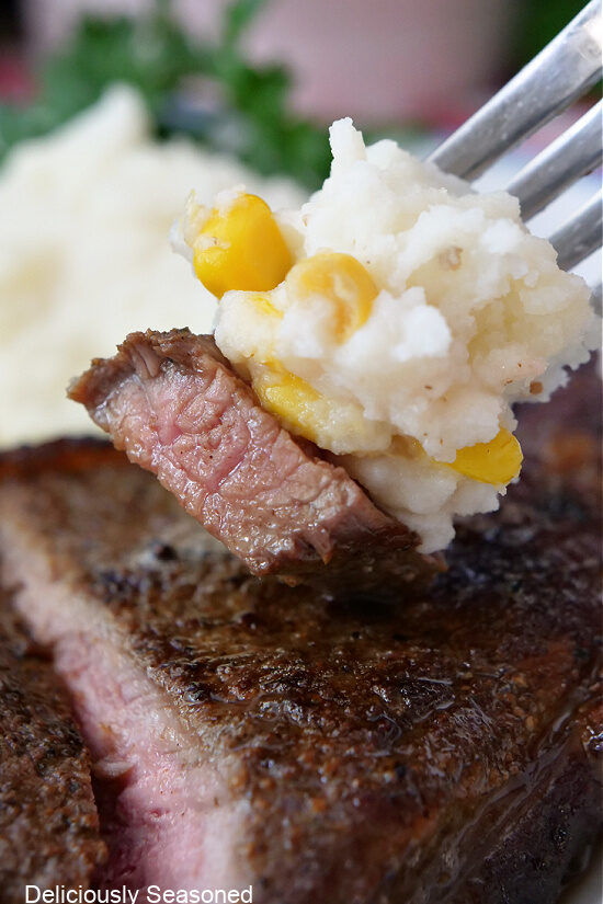 A close up of a bite of steak with mashed potatoes.
