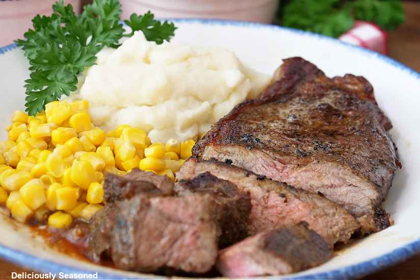 A white plate with steak, corn and mashed potatoes on it.