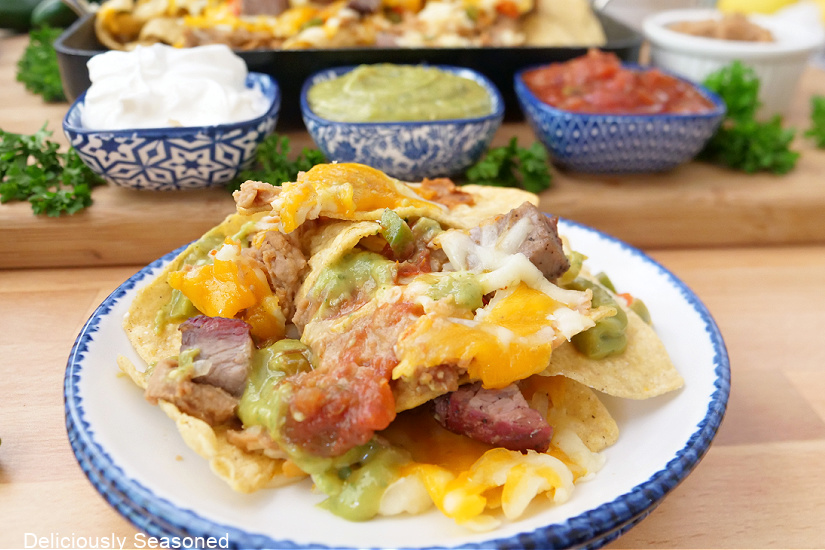 A horizontal photo of a white plate with blue trim with a serving of nachos on it.