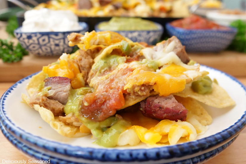 A horizontal photo of a serving of nachos on a white plate with blue trim.