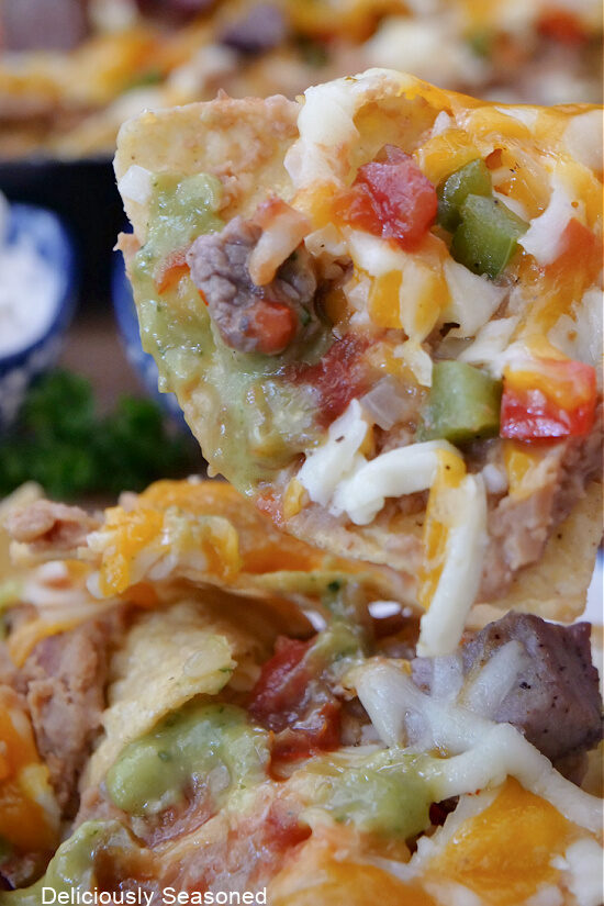 A close up of a tortilla chip filled with all the ingredients in classic steak nachos.