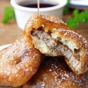 A close up of a sausage patty that has been covered in pancakes with syrup being drizzled over the top.
