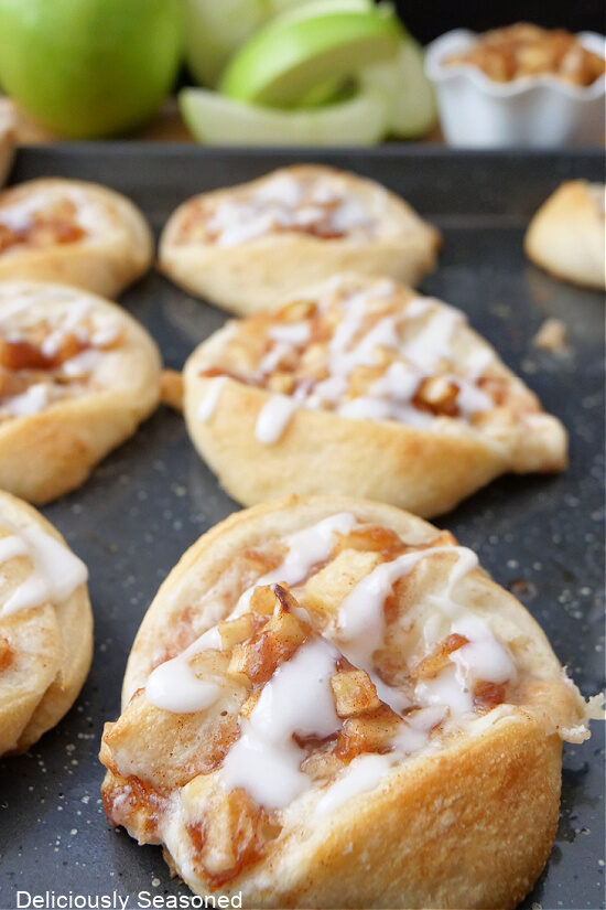 Apple cream cheese rolls on a baking sheet drizzled with glaze.