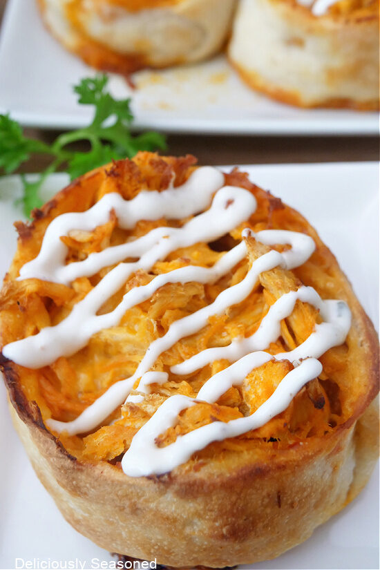 Close up photo of a white plate with a buffalo chicken pinwheel on it that is drizzled with ranch dressing.