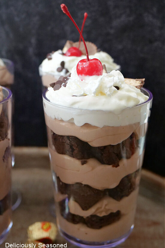 A close up of a chocolate pudding parfait with pieces of brownie, whipped cream and a cherry on top.