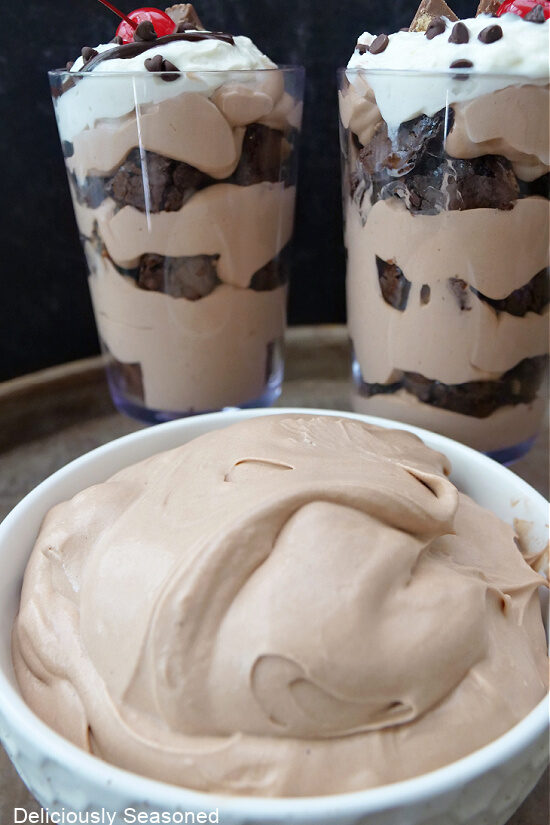 A white bowl filled with chocolate pudding and two parfaits in the background.