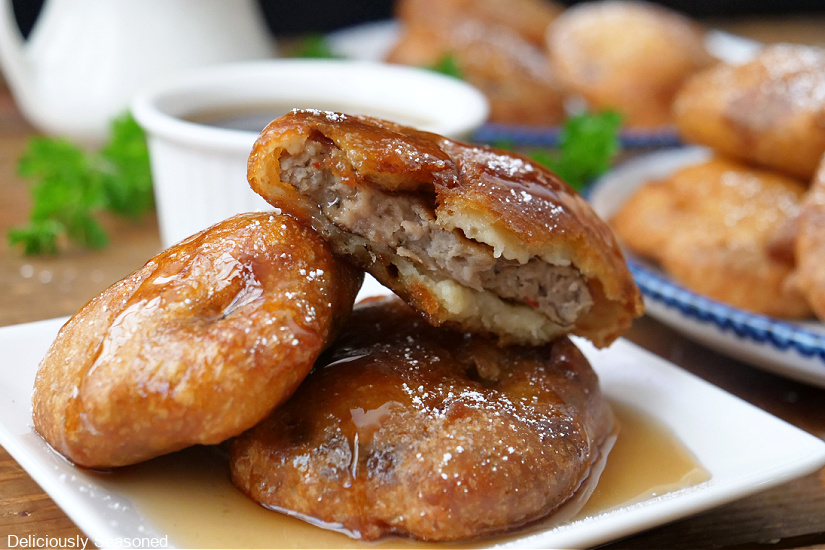 A horizontal photo of a white plate with three pancake sausage bites with more bites on two plates in the background.