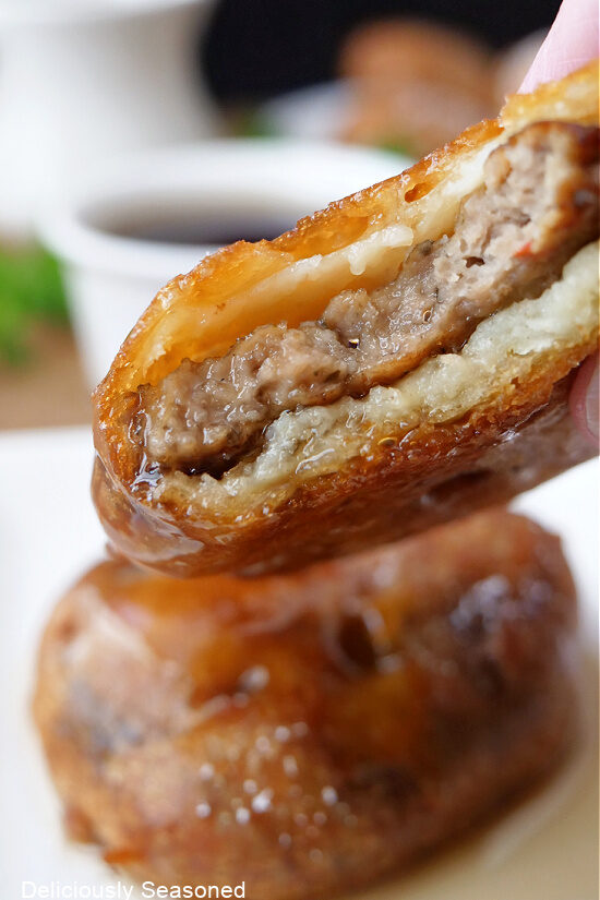 A close up of a sausage pancake bite that has a bite taken out of it and has been dipped in syrup.